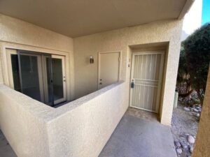 Gated door to condo next to walled-in patio with sliding glass door.
